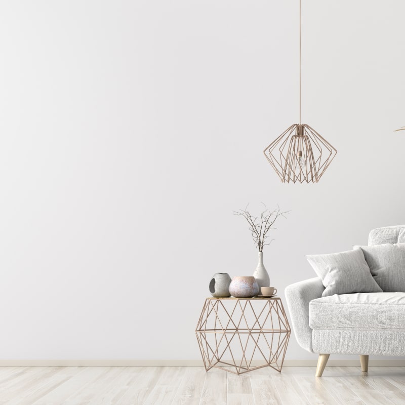 Salon scandinave minimaliste : décor clair et design moderne Intérieur minimaliste blanc avec canapé gris clair, table d'appoint géométrique en cuivre, suspension design et vase avec brindilles sèches.