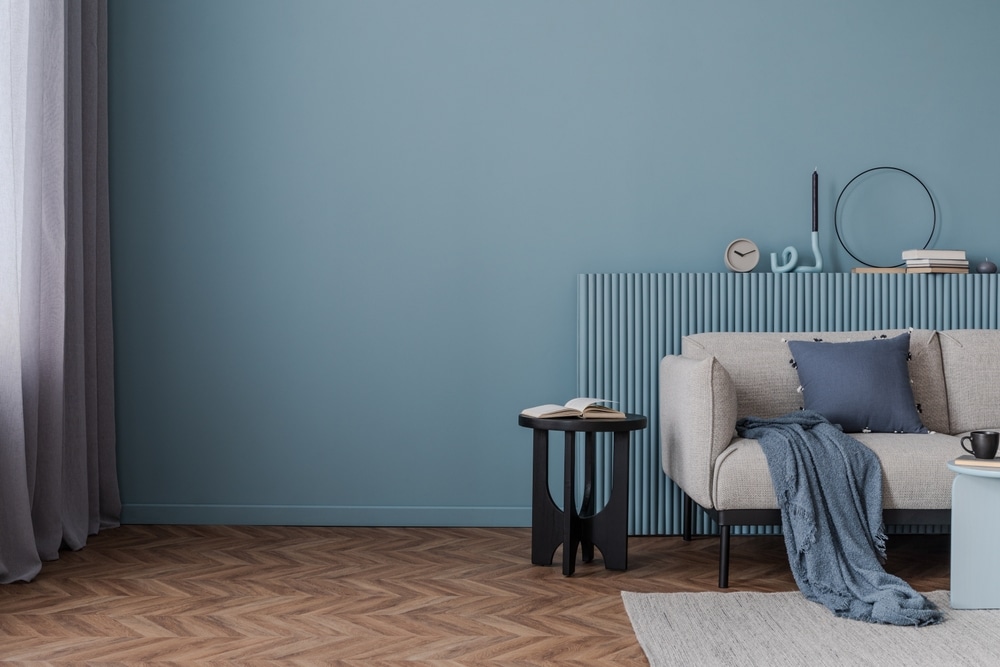 Salon moderne bleu sarcelle : Idées de décoration murale. Intérieur moderne. Mur bleu sarcelle et panneau flûté derrière un canapé beige. Plancher chevrons, table noire, et jeté bleu.